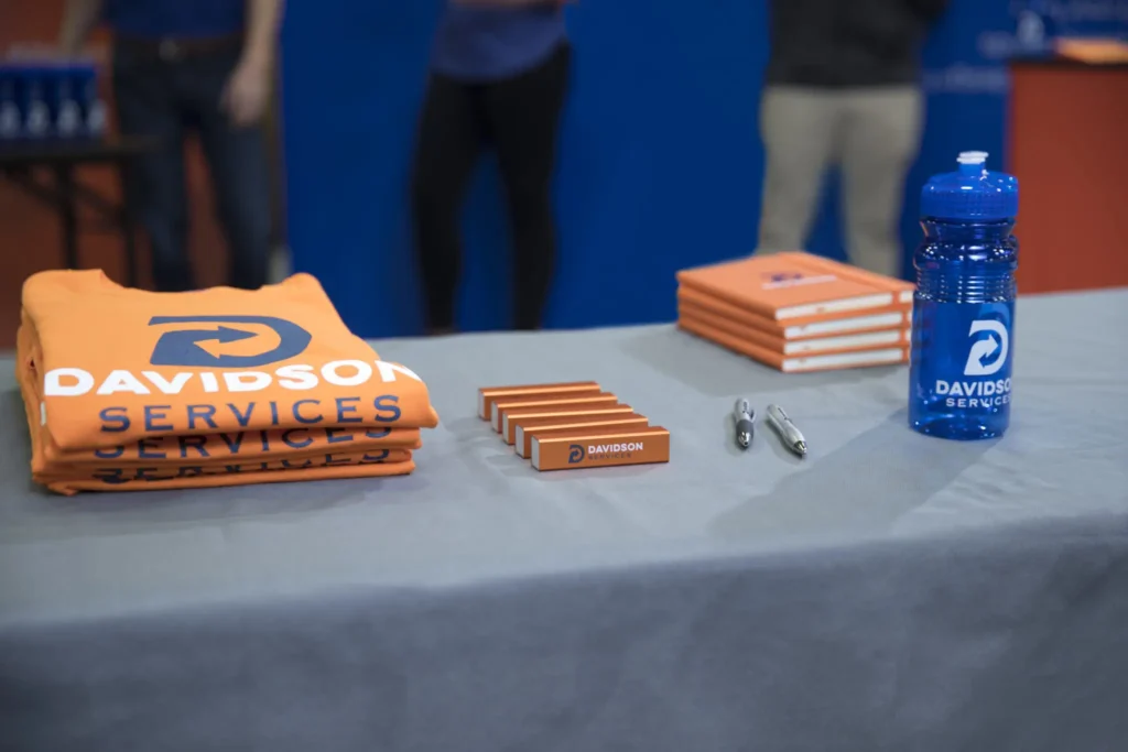 trade show display booth with custom apparel, pens, notebooks, and water bottles